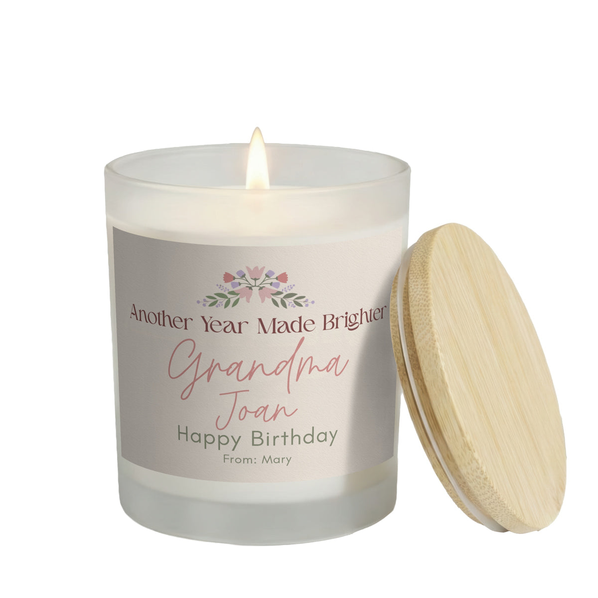 Another Year Made Brighter personalized frosted candle, lit with the bamboo lid set aside, on a white background
