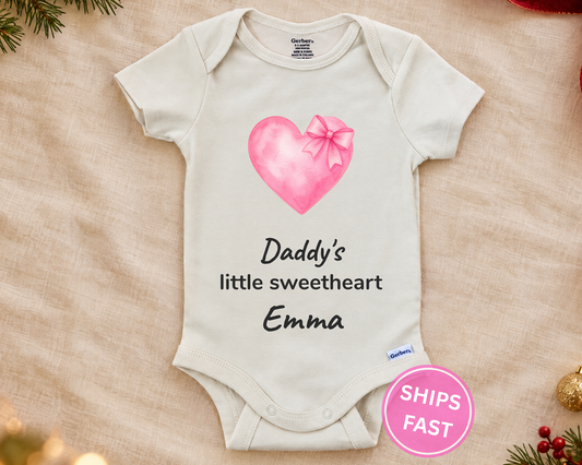 Daddy's Little Sweetheart personalized baby bodysuit with pink watercolor heart and bow on a cream blanket