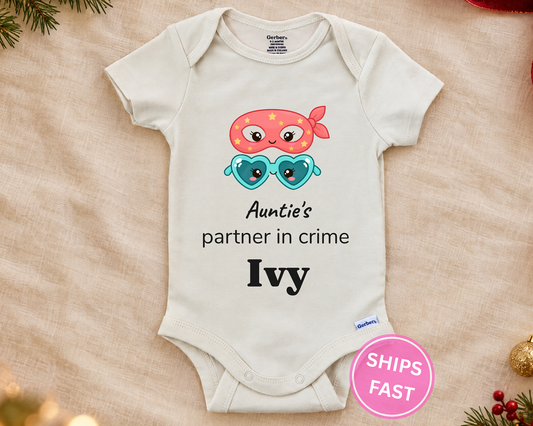 Auntie's Partner in Crime personalized baby bodysuit with bandit mask and heart sunglasses on a cream blanket