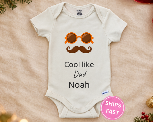 Cool Like Dad personalized baby bodysuit with orange sunglasses and mustache on a cream blanket