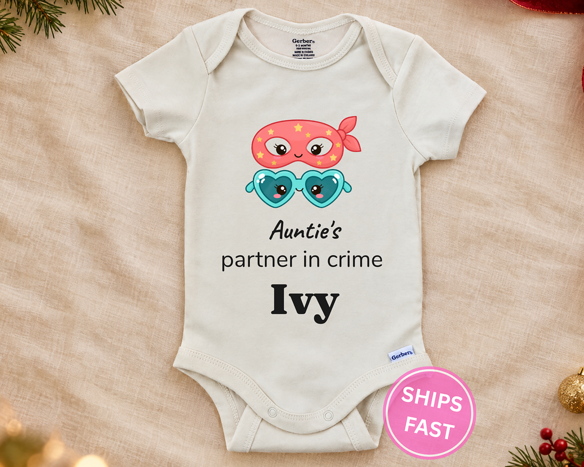 Auntie's Partner in Crime personalized baby bodysuit with bandit mask and heart sunglasses on a cream blanket