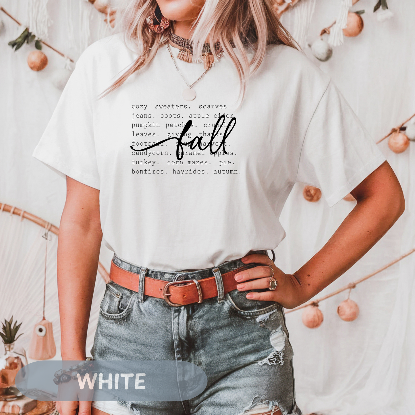 Model wearing a white cozy fall tee with autumn words, surrounded by fall decorations.